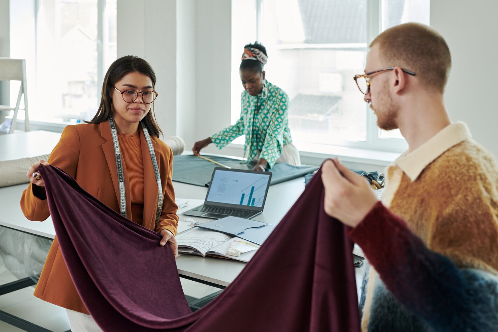 Male and female fashion designers folding wide piece of purple velvet or other textile while working over new seasonal collection