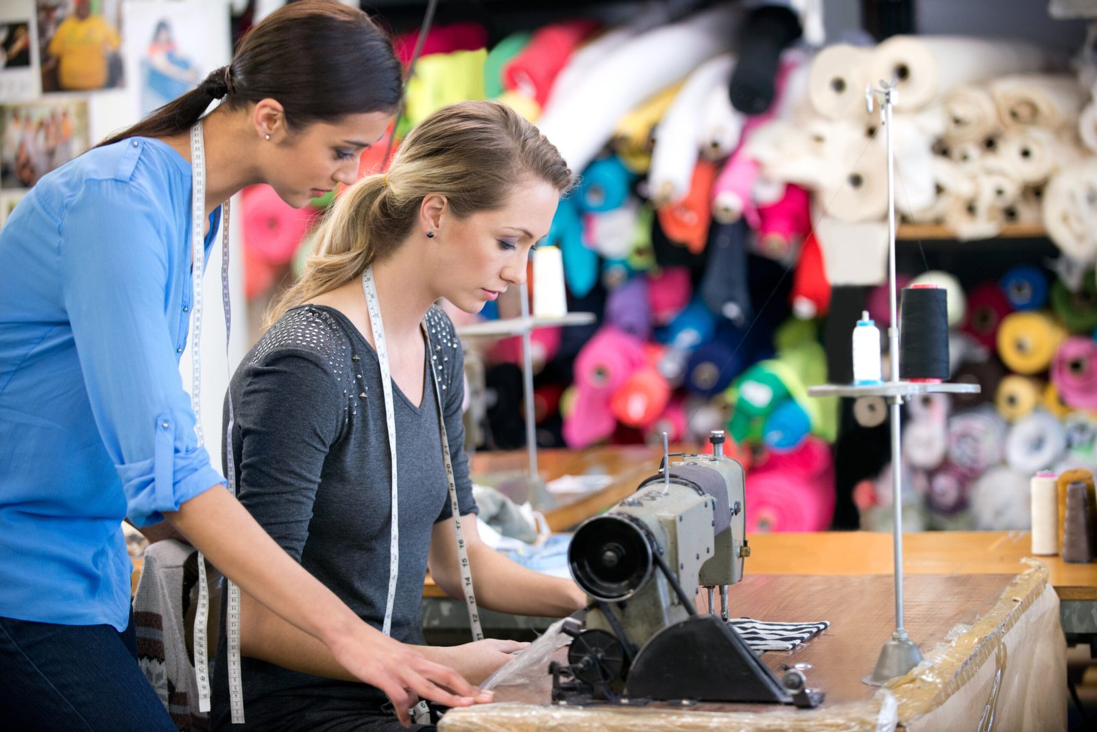 Two women working on a garment at a workbench inside their fabric shop.