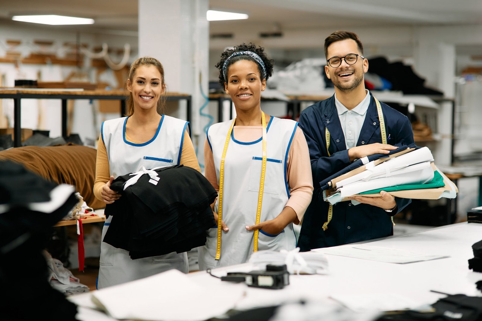 Multiracial group of happy textile workers at tailor's looking at camera.